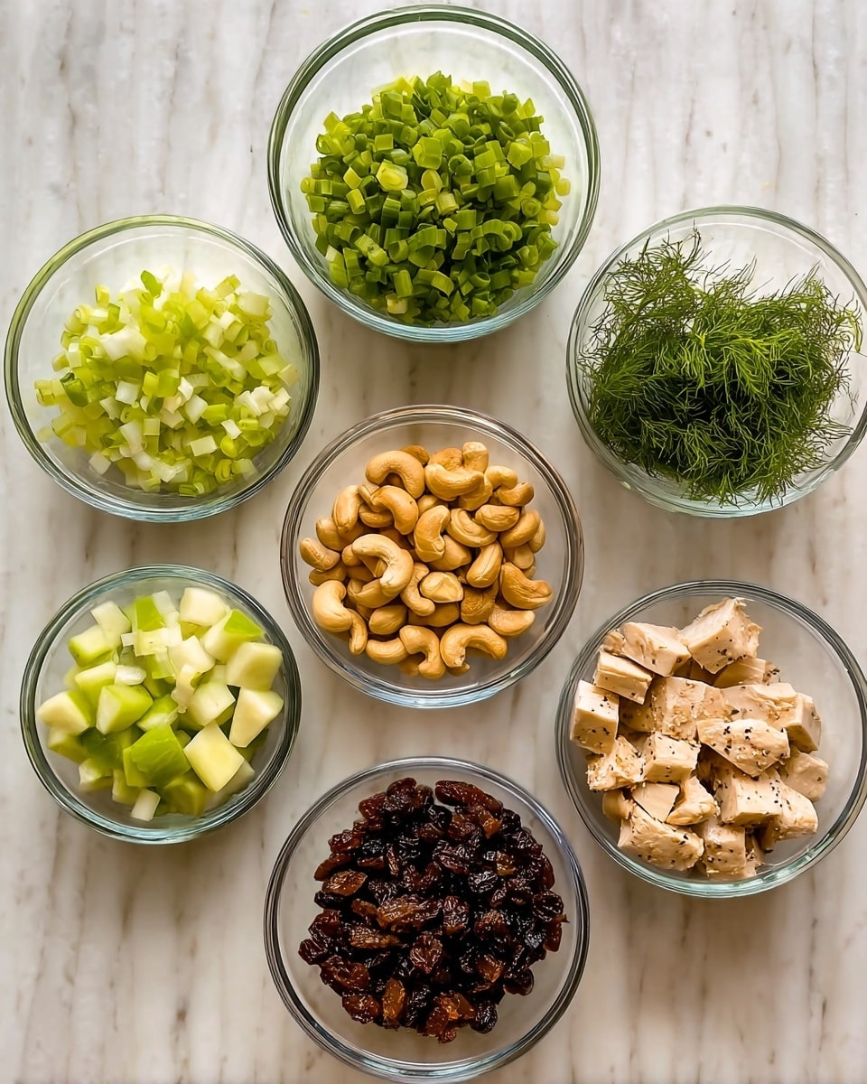 Seven small clear glass bowls are arranged on a white marbled surface. Starting from the top left, the first bowl contains chopped green onions with a fresh, vibrant green color. To the right of it, there is a bowl filled with thin green dill leaves, giving a feathery texture. Below the green onions, a bowl holds golden cashew nuts with a smooth, curved shape. In the center, there is a bowl of dark brown raisins with a wrinkled texture. To the right of the raisins, a bowl has small, diced light green celery pieces. On the bottom left, a bowl contains diced green apple chunks with a shiny, crisp look. The largest bowl to the bottom right contains cubed pieces of cooked pale beige chicken seasoned lightly with pepper. Photo taken with an iphone --ar 4:5 --v 7