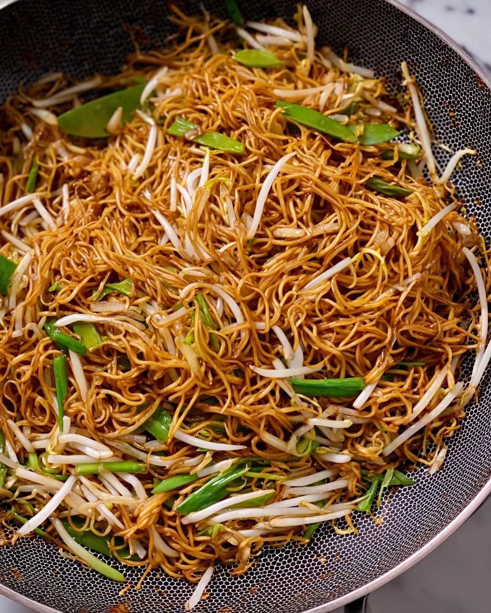 The image shows a close-up of a pan filled with stir-fried noodles. The noodles are thin and golden brown, mixed with long white bean sprouts and some bright green scallions scattered throughout. The pan has a textured dark gray inner surface with a honeycomb pattern. The noodles appear evenly cooked with a slight shine, blending well with the crisp vegetables within the pan. The background is a white marbled surface. photo taken with an iphone --ar 4:5 --v 7