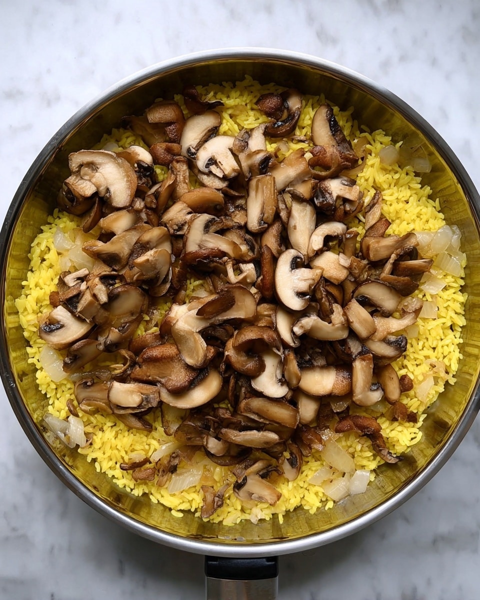 A pan with yellow rice spread evenly in the bottom layer, cooked with small pieces of translucent onions visible within the rice. On top of the rice is a thick layer of roughly chopped brown mushrooms, showing both caps and stems. The mushrooms contrast with the bright yellow rice under them, and the pan sits on a white marbled surface. photo taken with an iphone --ar 4:5 --v 7