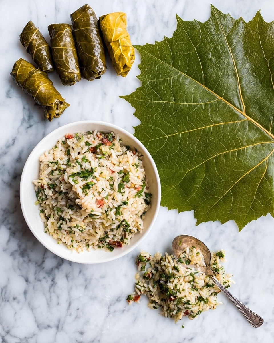 A white bowl filled with cooked rice mixed with finely chopped herbs and small bits of vegetables sits on a white marbled surface. To the right, a large green grape leaf is spread flat with a small mound of the rice mixture placed in the center. A silver spoon with some rice mixture rests nearby on the marble. In the upper left corner, five rolled grape leaves are placed in a small cluster, varying from dark green to yellow-green in color, showing the stages before and after rolling. Photo taken with an iphone --ar 4:5 --v 7