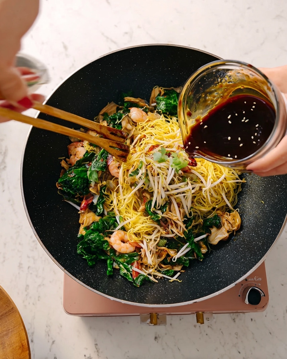 A close-up view of a black wok filled with cooked yellow noodles mixed with bright green leafy vegetables, light brown cooked pieces of chicken, pink shrimp, and white bean sprouts. A woman's hand is pouring a thick dark brown sauce from a clear glass bowl into the wok. Another woman's hand is holding wooden chopsticks on the left side, stirring the ingredients. The wok is placed on a light pink portable stove, sitting on a white marbled surface. photo taken with an iphone --ar 4:5 --v 7