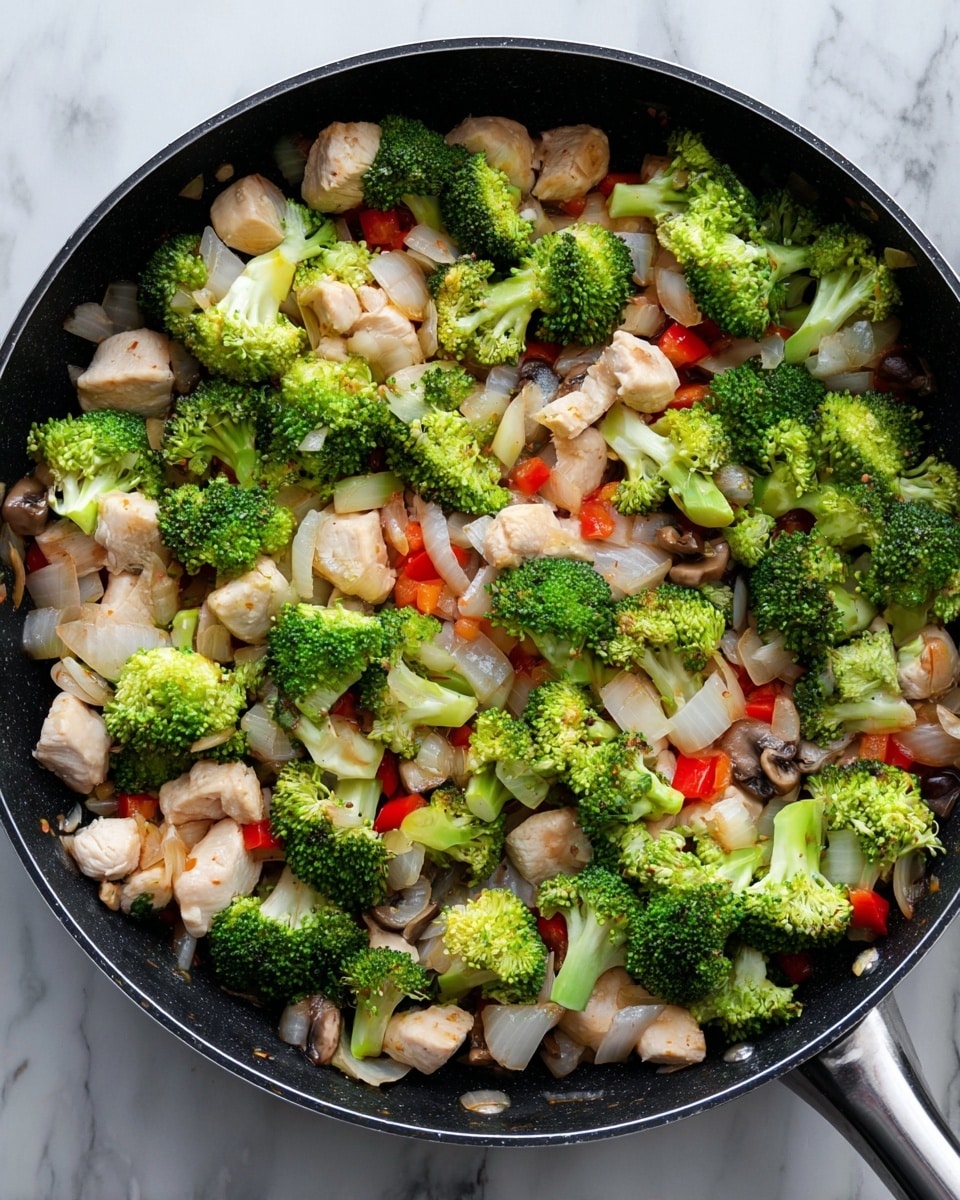 A black pan filled with a stir fry showing three main layers: the bottom layer has small chunks of white cooked chicken, mixed with small pieces of white onion and tiny cubes of red bell pepper; the middle layer includes a light scattering of thinly sliced cooked mushrooms blending with the chicken and vegetables; the top layer is bright green broccoli florets spread evenly over the dish. The pan is placed on a white marbled surface. photo taken with an iphone --ar 4:5 --v 7