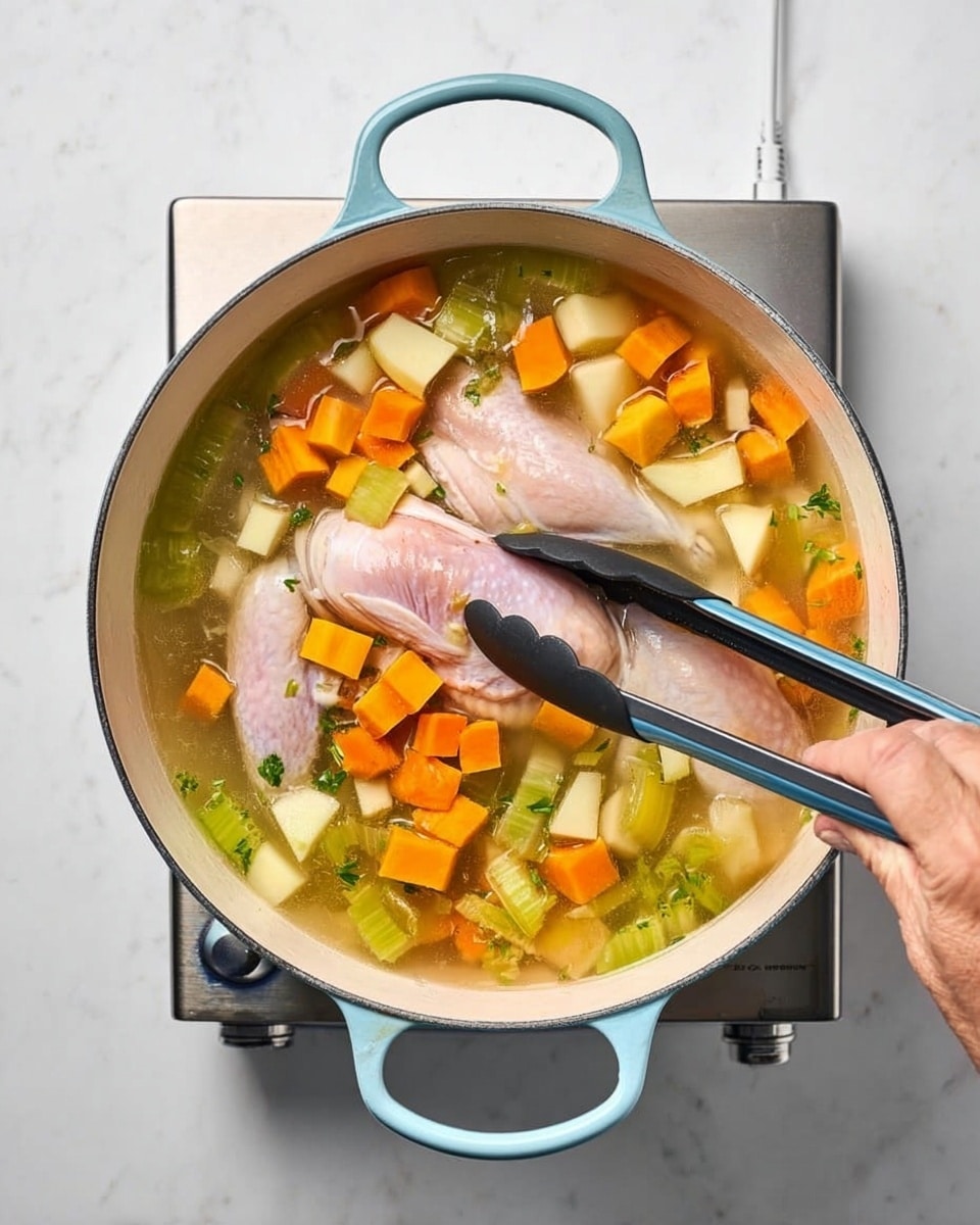 A white pot with light blue handles sits on a small silver burner over a white marbled surface, filled with a clear broth containing large pieces of raw light pink chicken submerged in the liquid. Around the chicken, there are diced orange sweet potatoes, pale yellow potatoes, green celery, and white onions, all floating and mixed evenly in the broth. A woman's hand is using black tongs to hold and place the chicken inside the pot. The scene is brightly lit and viewed from above, showing the colors and textures clearly. photo taken with an iphone --ar 4:5 --v 7