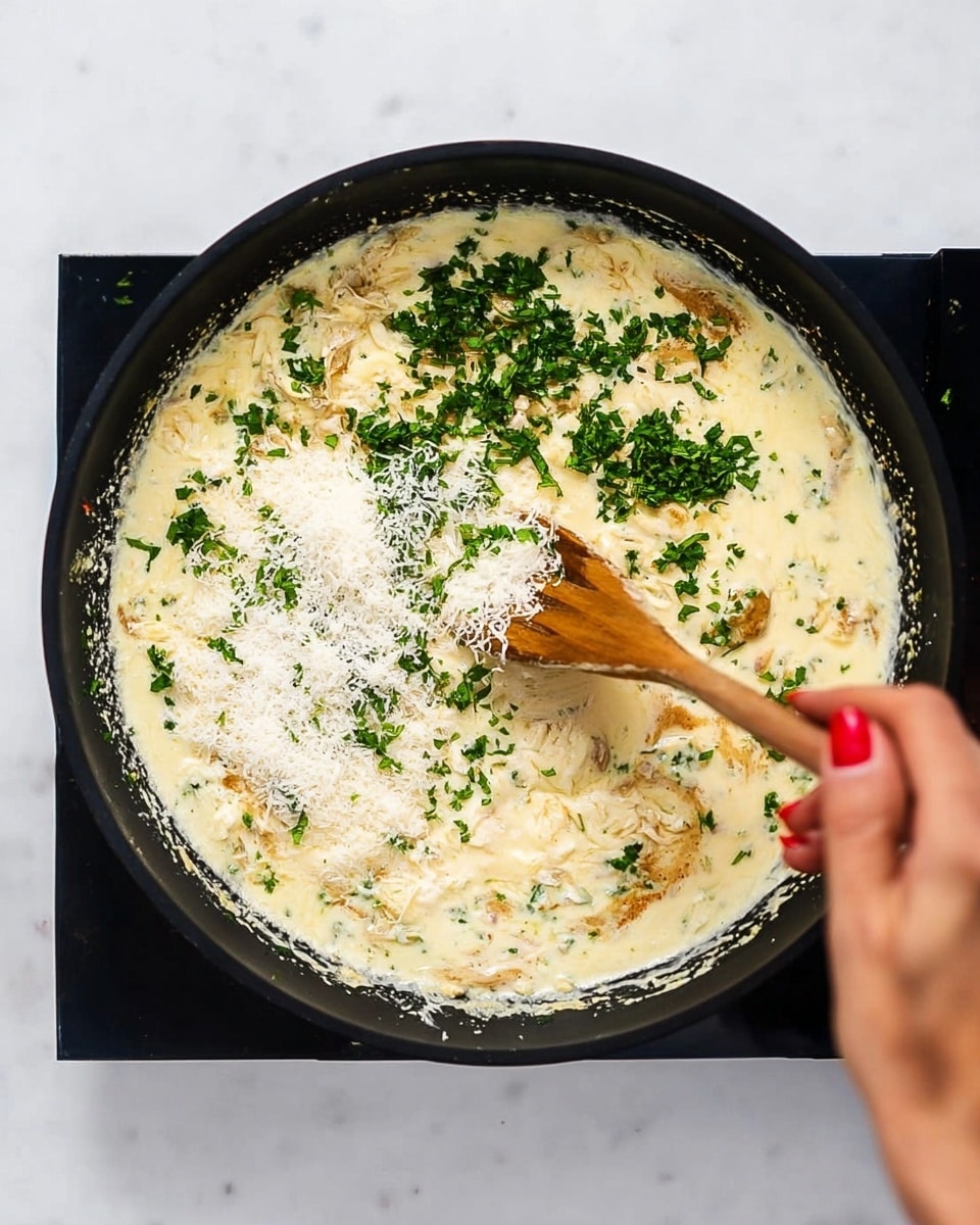 A black pan sits on a white marbled surface filled with a creamy mixture that is pale yellow and thick, dotted with light brown browned pieces. On top, there are fresh green chopped herbs scattered unevenly across the surface, and a layer of finely grated white cheese sprinkled over. A woman's hand with red-painted nails holds a wooden spoon stirring the mixture gently from the right side. The pan edges are well defined against the clean white marbled background. photo taken with an iphone --ar 4:5 --v 7