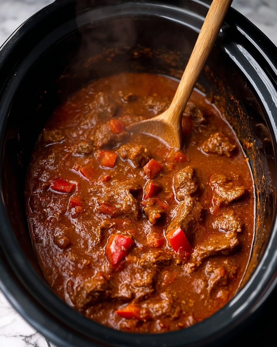This image shows a thick stew with rich reddish-brown sauce and chunks of tender meat and red bell pepper pieces, all mixed together in a black slow cooker. A wooden spoon is stirring the stew from the top left corner, with the sauce glistening and steam rising lightly, giving a warm and hearty feel. The stew's texture appears smooth with visible spices in the sauce, and the meat and peppers are spread evenly inside the pot. The background is a white marbled texture. photo taken with an iphone --ar 4:5 --v 7