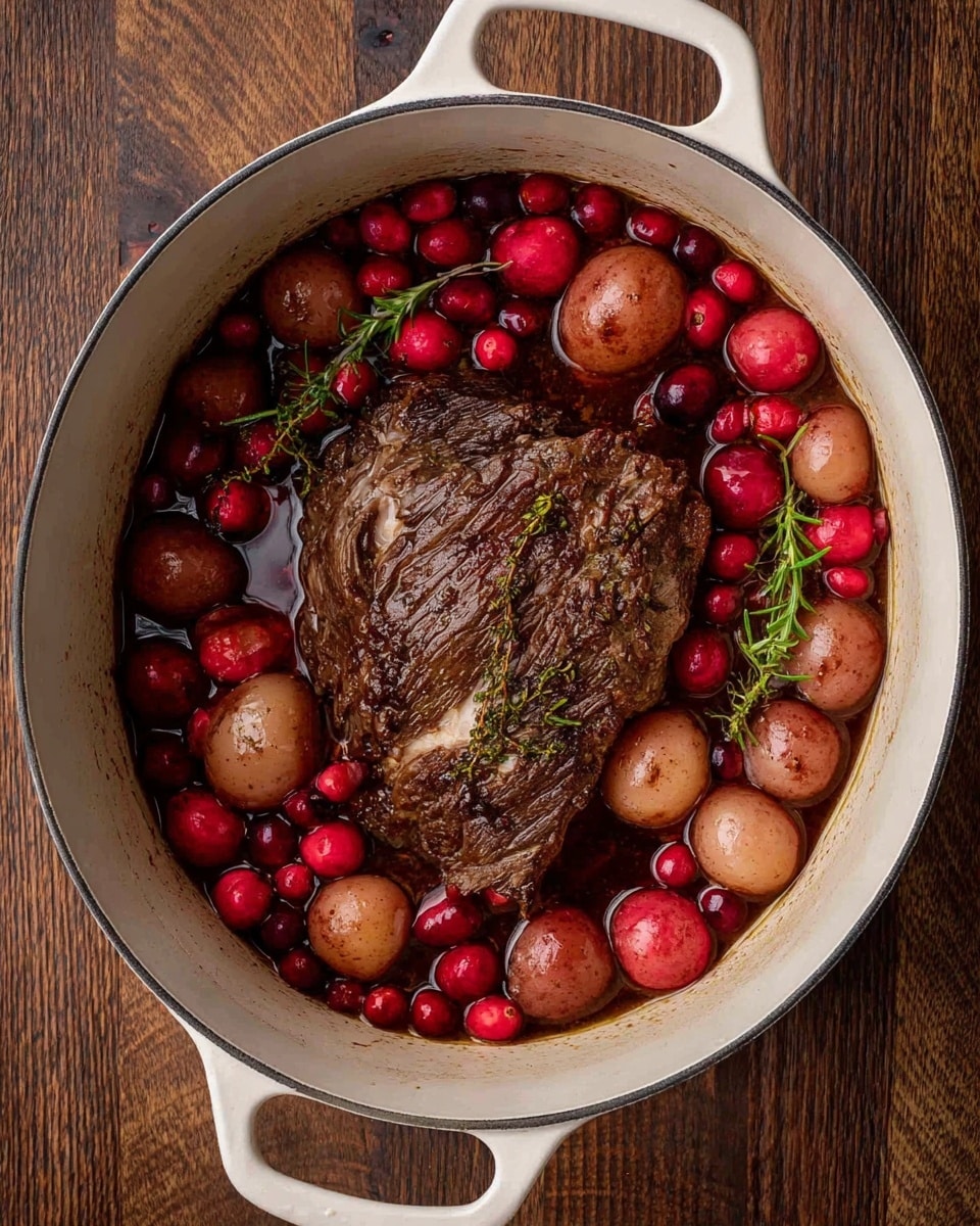 A white pot with two handles sits on a wooden surface, filled with a large piece of browned meat in the center, surrounded by small red potatoes and bright red fresh cranberries floating in a dark brown liquid with visible herbs like rosemary scattered throughout, creating a rich and hearty scene. Photo taken with an iphone --ar 4:5 --v 7