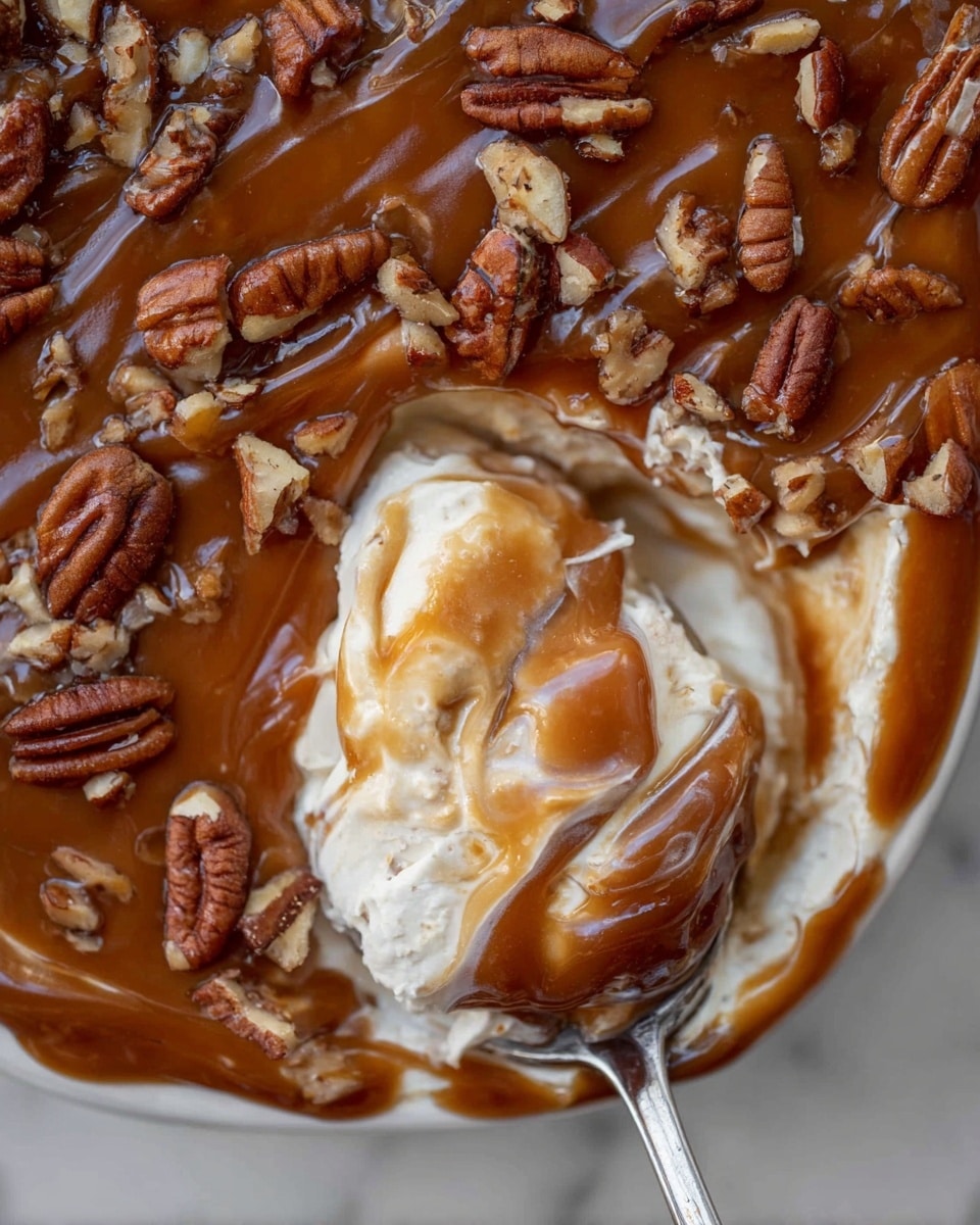 This image shows a close-up of a layered dessert in a white dish on a white marbled surface. The top layer is a smooth, shiny caramel brown sauce sprinkled with chopped pecans spread evenly across it. Below this is a thick, creamy off-white layer of whipped topping or cream, swirled gently with caramel sauce showing soft texture. A silver spoon is scooping into the dessert, lifting up a portion that reveals the two distinct layers. The pecans add a rough texture on top in contrast to the smooth caramel and creamy layers below. photo taken with an iphone --ar 4:5 --v 7